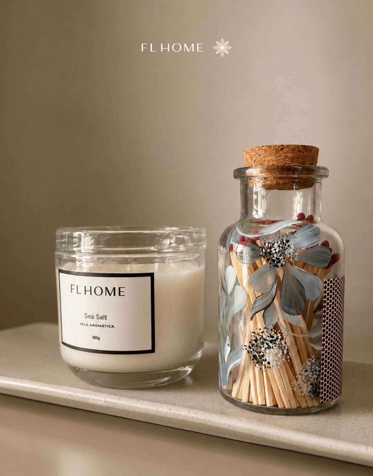 Vela aromática Sea Salt da FL Home ao lado de um frasco de fósforos decorado com flores, com a marca FL Home na parte superior.