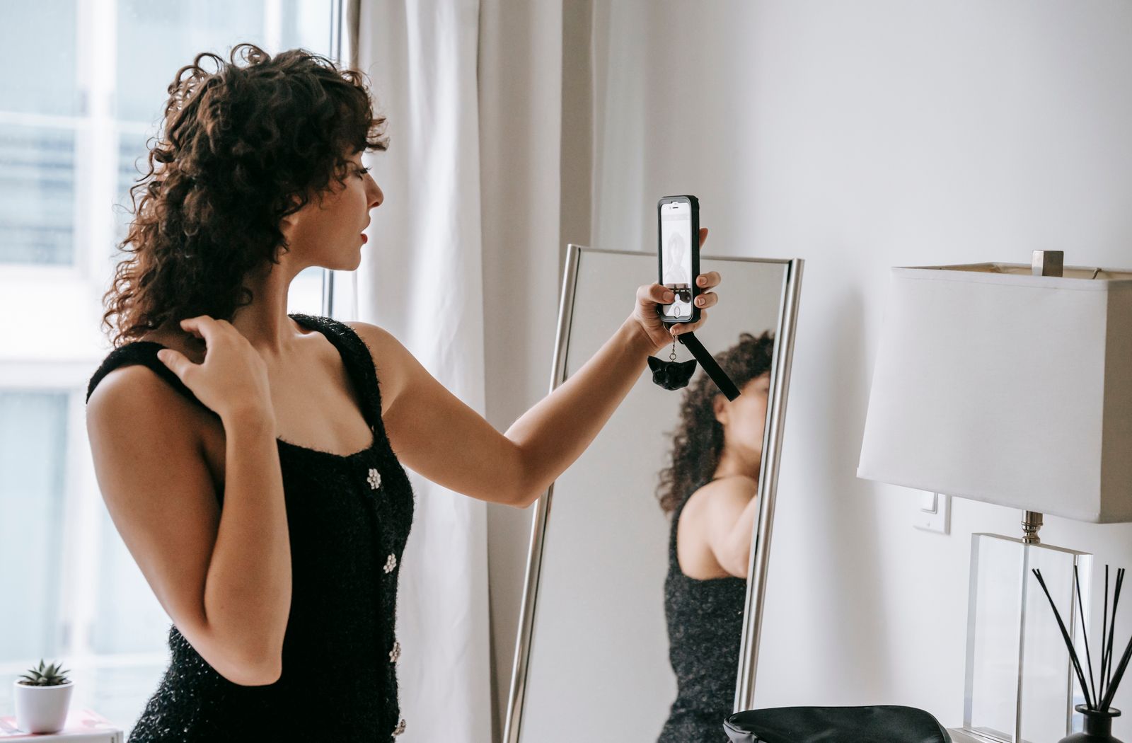 Mulher usando o celular para fotografar seu reflexo no espelho.